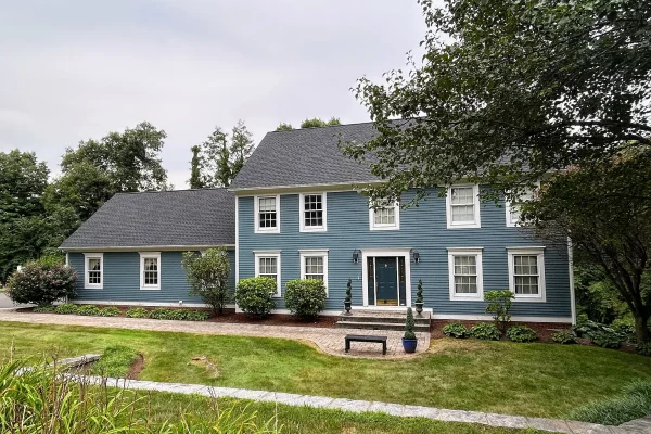 Front view of a large two-story colonial-style home with blue clapboard siding, a black roof, and a well-maintained lawn and landscaping in Farmington, CT.