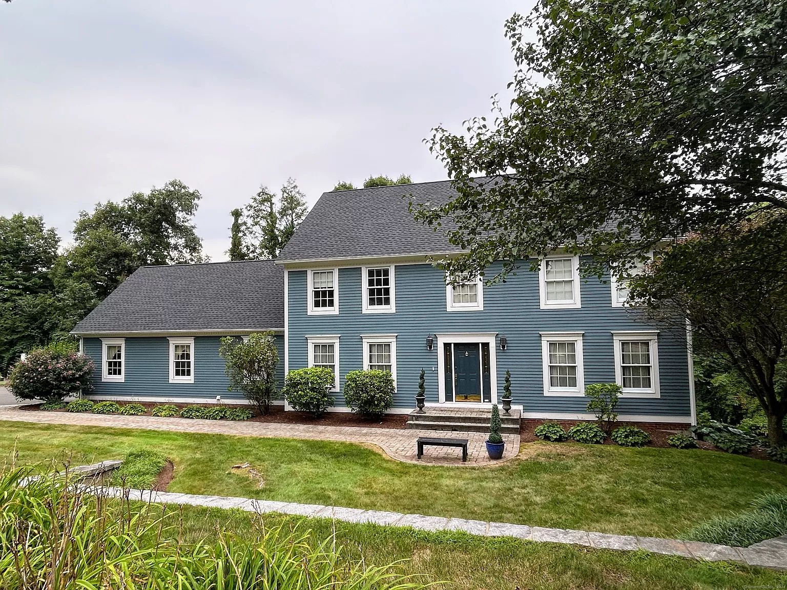 Front view of a large two-story colonial-style home with blue clapboard siding, a black roof, and a well-maintained lawn and landscaping in Farmington, CT.