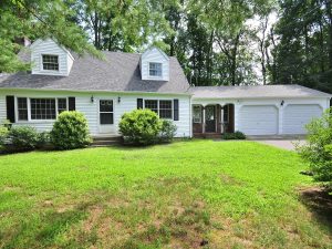 A white Cape Cod-style house at 1 Burlington Road, Unionville, CT 06085, with a well-maintained lawn, black shutters, and a two-car garage surrounded by trees.