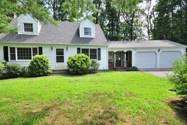 A white Cape Cod-style house at 1 Burlington Road, Unionville, CT 06085, with a well-maintained lawn, black shutters, and a two-car garage surrounded by trees.