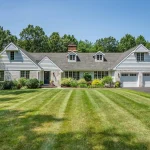Front view of a beautifully landscaped white ranch-style home with a well-maintained lawn and attached garage in Farmington, CT