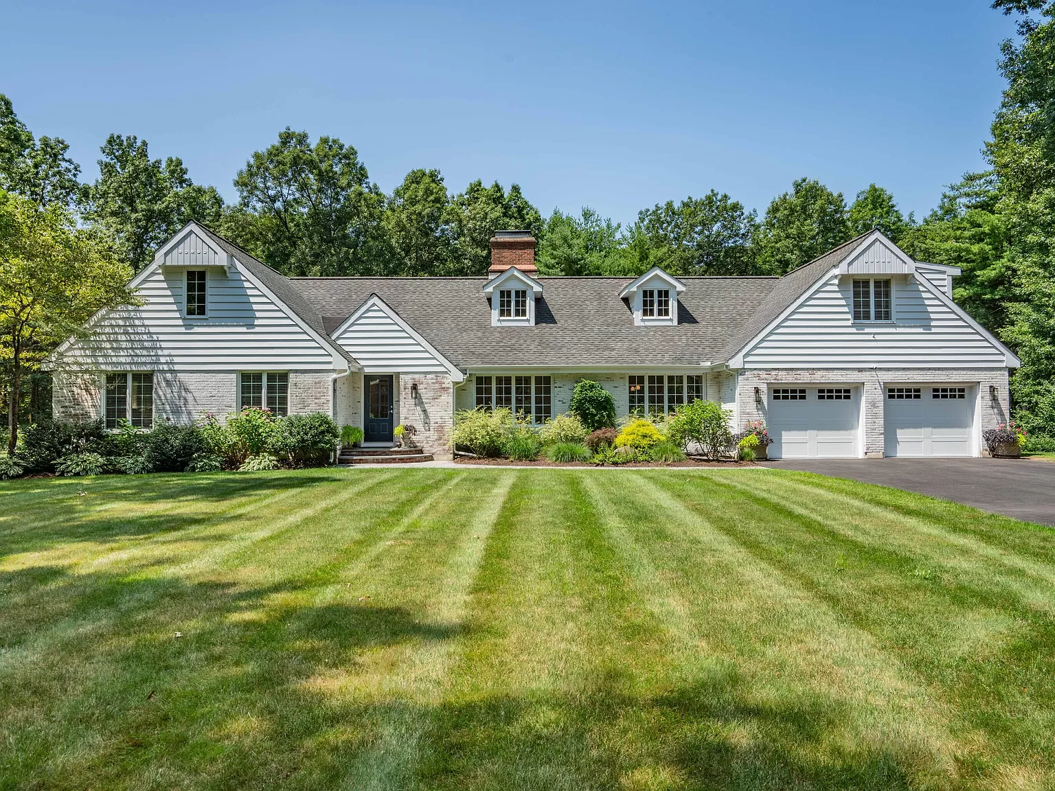 Front view of a beautifully landscaped white ranch-style home with a well-maintained lawn and attached garage in Farmington, CT