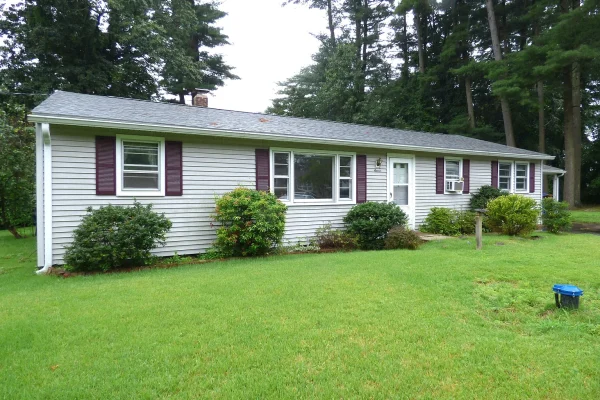 Single-story ranch-style home with gray vinyl siding and burgundy shutters in Farmington, CT, surrounded by lush green grass and mature trees.