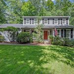 Colonial-style home with a red door and American flag at 10 Deepwood Drive, Farmington, CT, surrounded by lush greenery.