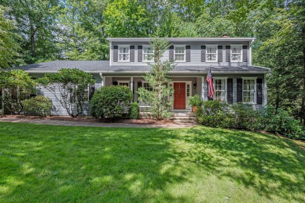 Colonial-style home with a red door and American flag at 10 Deepwood Drive, Farmington, CT, surrounded by lush greenery.