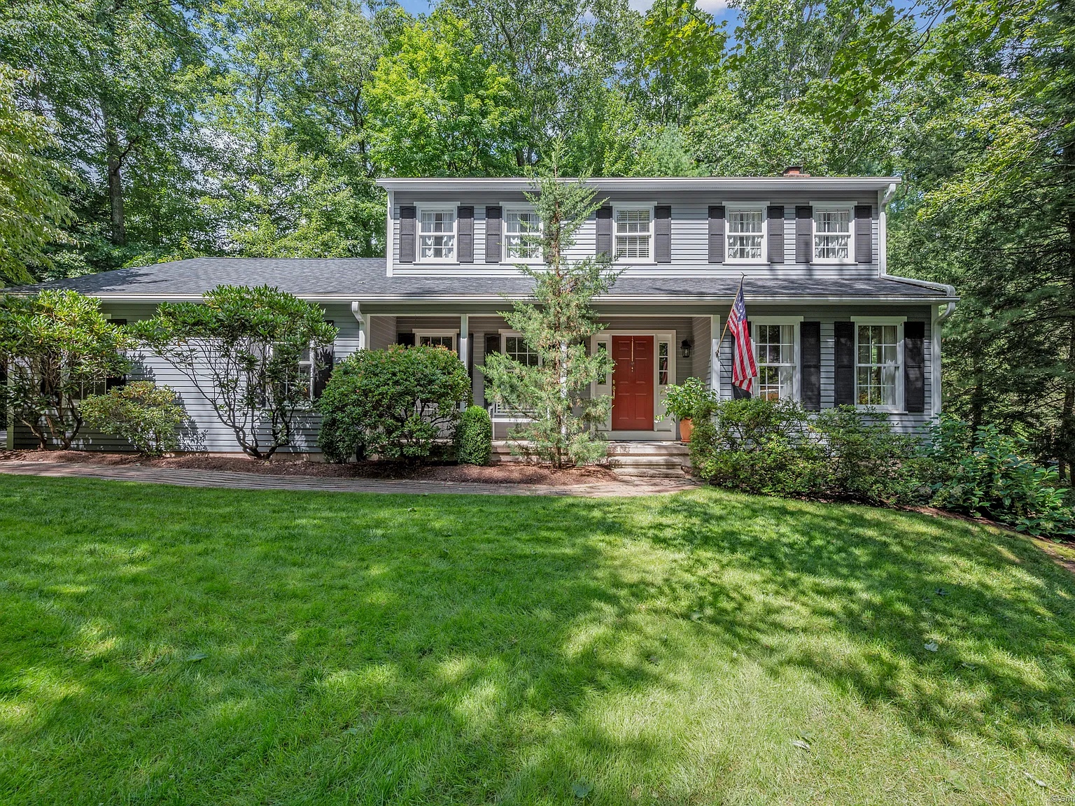 Colonial-style home with a red door and American flag at 10 Deepwood Drive, Farmington, CT, surrounded by lush greenery.