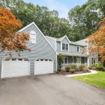 Front exterior view of a charming two-story colonial home with a two-car garage at 12 Village View Ln, Unionville, CT, surrounded by autumn trees.