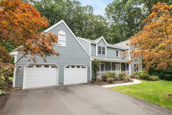 Front exterior view of a charming two-story colonial home with a two-car garage at 12 Village View Ln, Unionville, CT, surrounded by autumn trees.