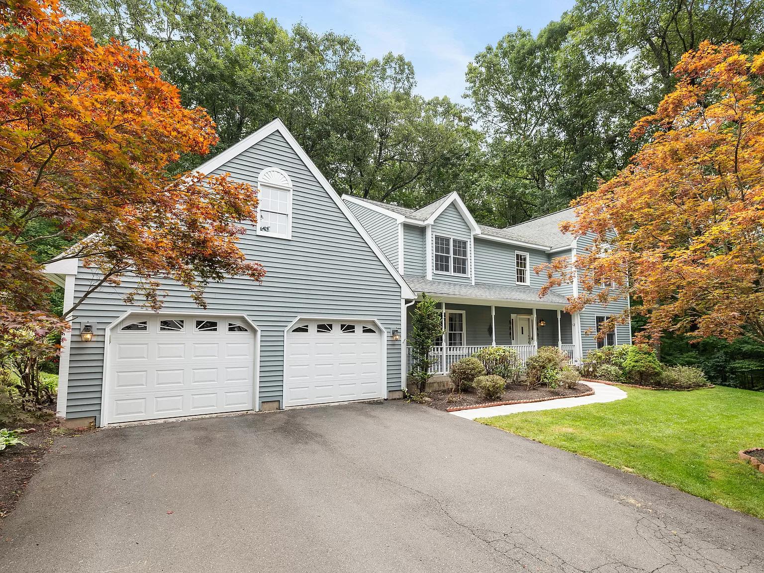 Front exterior view of a charming two-story colonial home with a two-car garage at 12 Village View Ln, Unionville, CT, surrounded by autumn trees.