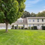 Front view of a large colonial-style house with a three-car garage and well-maintained lawn at 9 Juniper Lane, Farmington, CT.