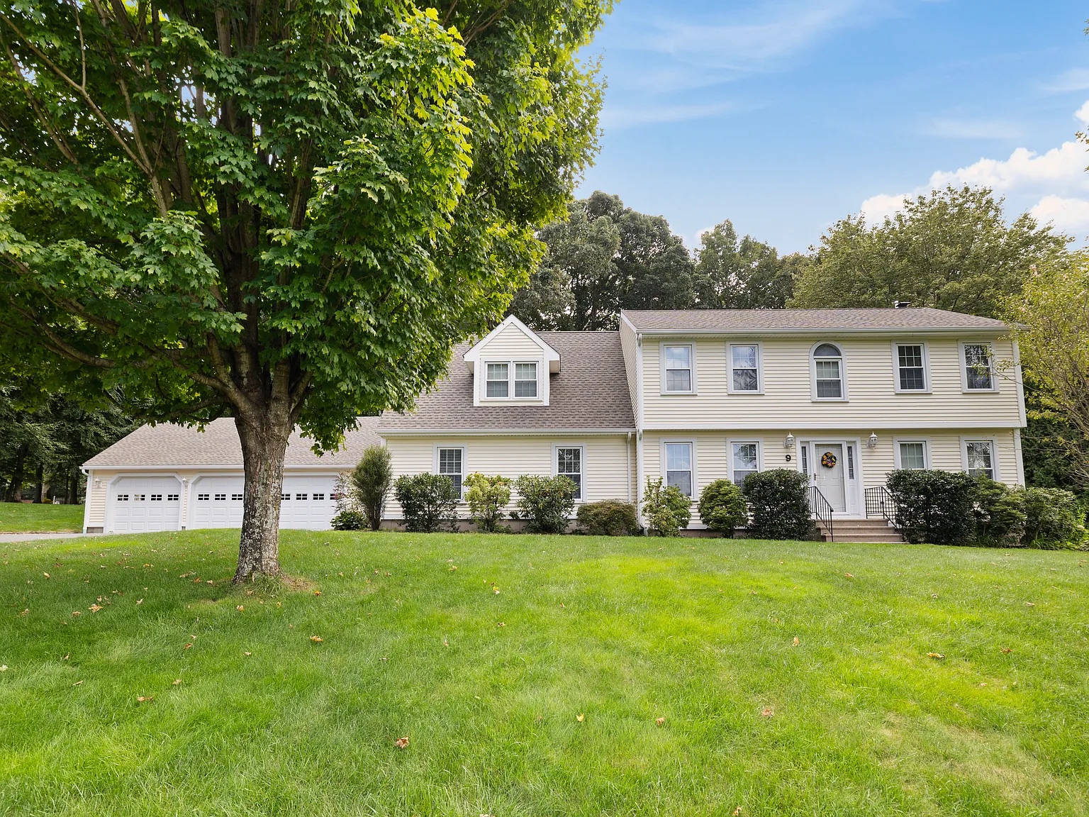 Front view of a large colonial-style house with a three-car garage and well-maintained lawn at 9 Juniper Lane, Farmington, CT.