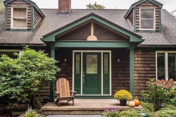 A charming front porch at 293 Old Mountain Rd, Farmington, CT, featuring green trim, a welcoming Adirondack chair, and a beautifully landscaped entrance with seasonal flowers and pumpkins.