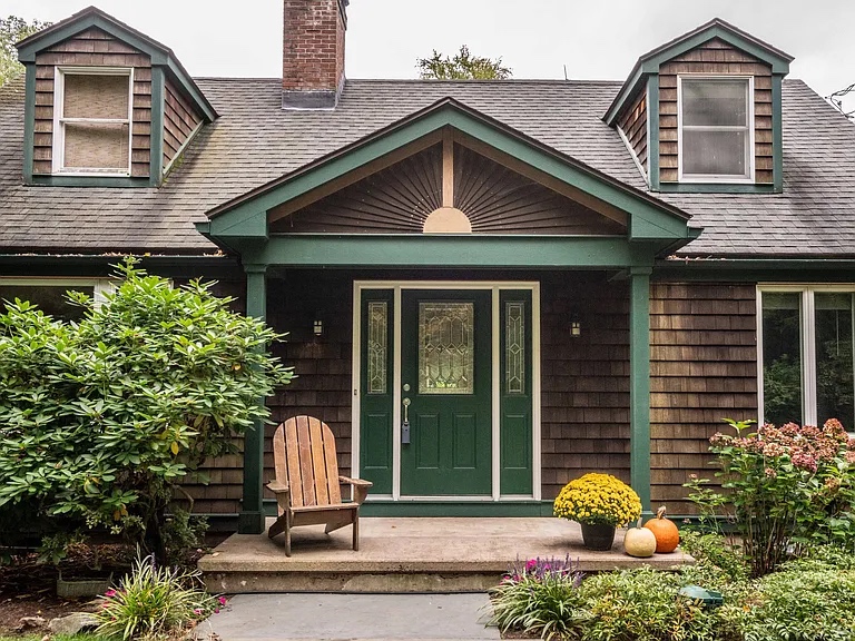 A charming front porch at 293 Old Mountain Rd, Farmington, CT, featuring green trim, a welcoming Adirondack chair, and a beautifully landscaped entrance with seasonal flowers and pumpkins.