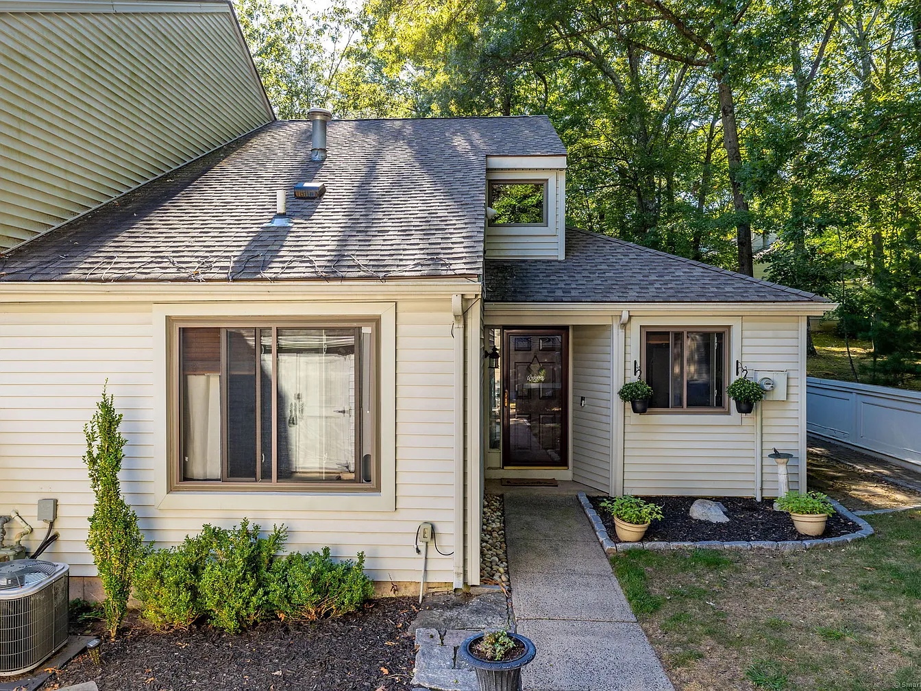 Front view of a cozy, two-story townhouse with light siding at 125 Farmington Chase Cres #125, Farmington, CT 06032, featuring a small garden and entryway.