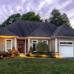 Exterior view of a luxury home at 19 Chimney Hill Dr, Farmington, CT 06032, featuring a two-car garage, well-manicured lawn, and warm exterior lighting at twilight.