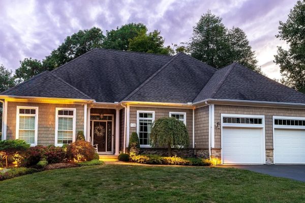 Exterior view of a luxury home at 19 Chimney Hill Dr, Farmington, CT 06032, featuring a two-car garage, well-manicured lawn, and warm exterior lighting at twilight.