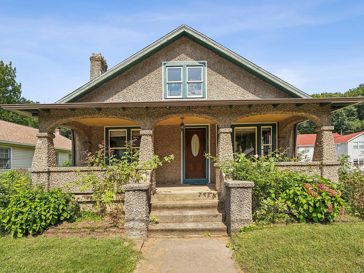 1920s bungalow at 1690 Farmington Avenue, Unionville, CT, featuring a charming front porch with unique stonework and lush greenery.