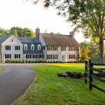 Front exterior of the Colonial estate at 325 Old Mountain Rd, Farmington, CT 06032, with a long driveway and expansive green lawns surrounded by trees.