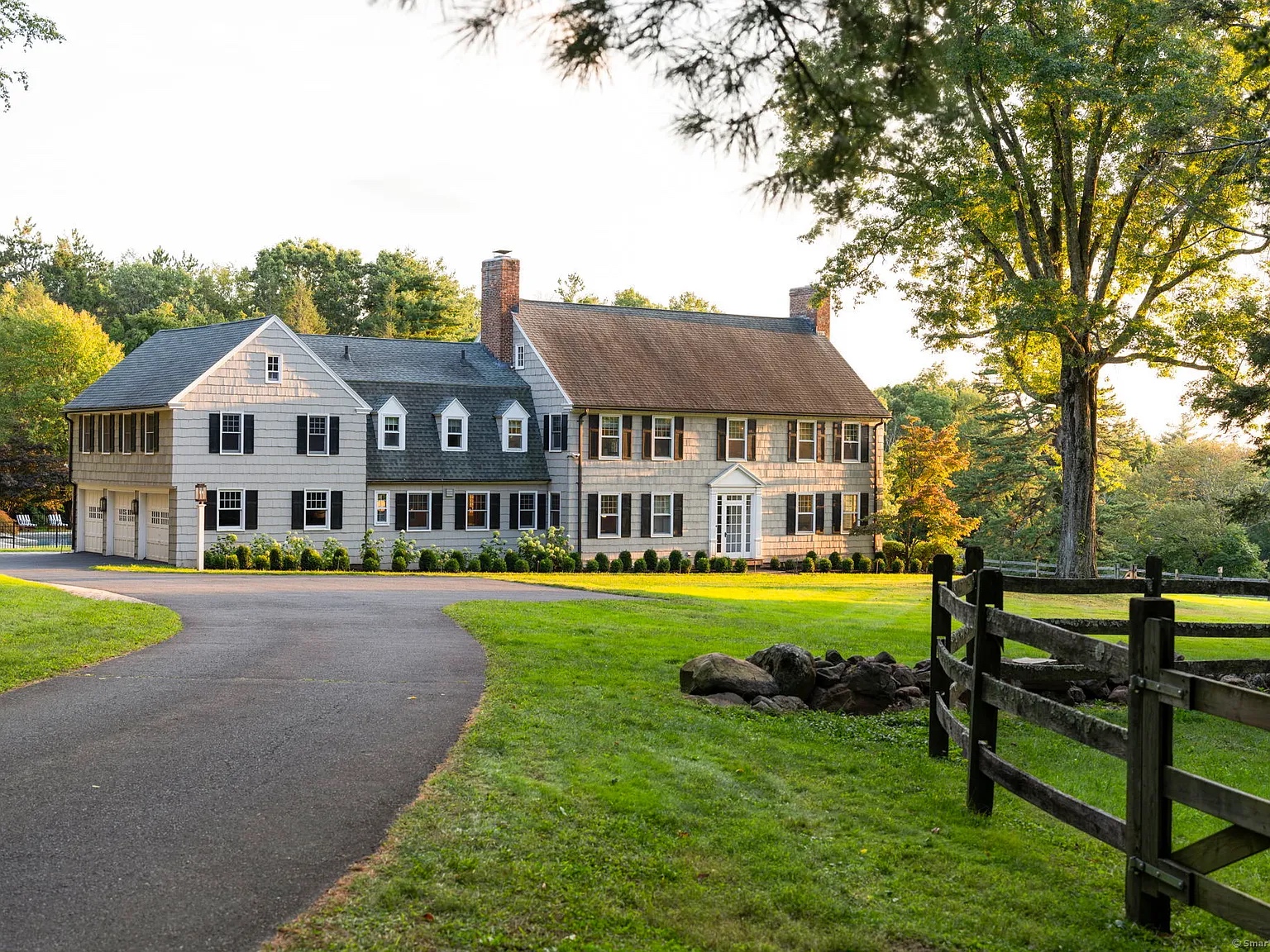 Front exterior of the Colonial estate at 325 Old Mountain Rd, Farmington, CT 06032, with a long driveway and expansive green lawns surrounded by trees.