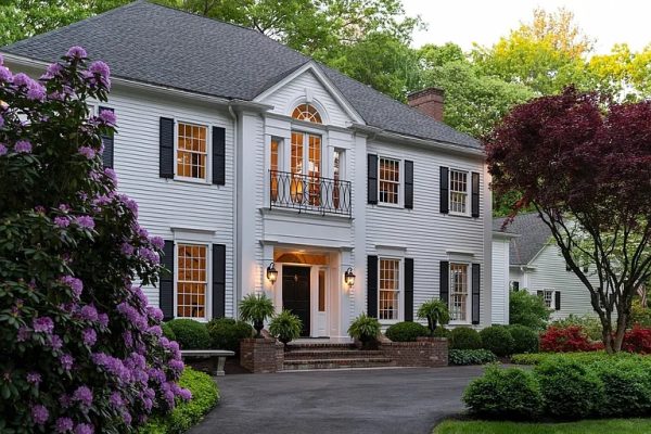 Elegant Georgian Colonial-style home at 11 Salisbury Way, Farmington, CT, featuring white clapboard siding, black shutters, and manicured landscaping with vibrant greenery and purple flowering shrubs.