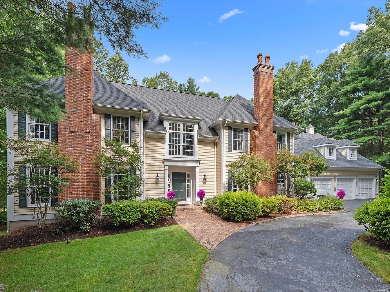 Exterior view of a luxury colonial-style home at 4 Pembroke Hill, Farmington, CT, featuring brick chimneys, manicured landscaping, and a three-car garage.